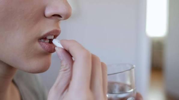 Mulher levando um comprimido à boca com um copo de água na mão