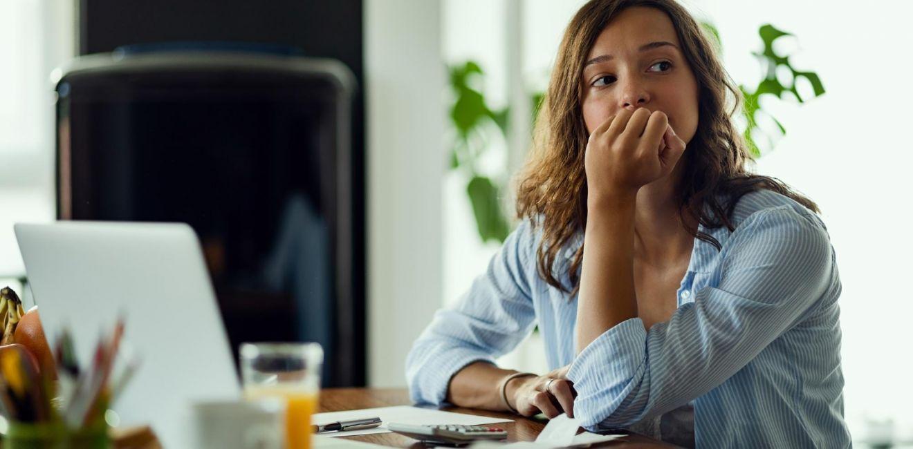 Mulher pensativa apoiada na mesa de trabalho, com o olhar distante