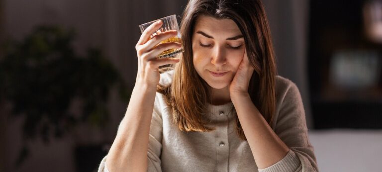 Mulher desolada com copo de bebida alcoólica na mão, possivelmente sofre com o alcoolismo feminino