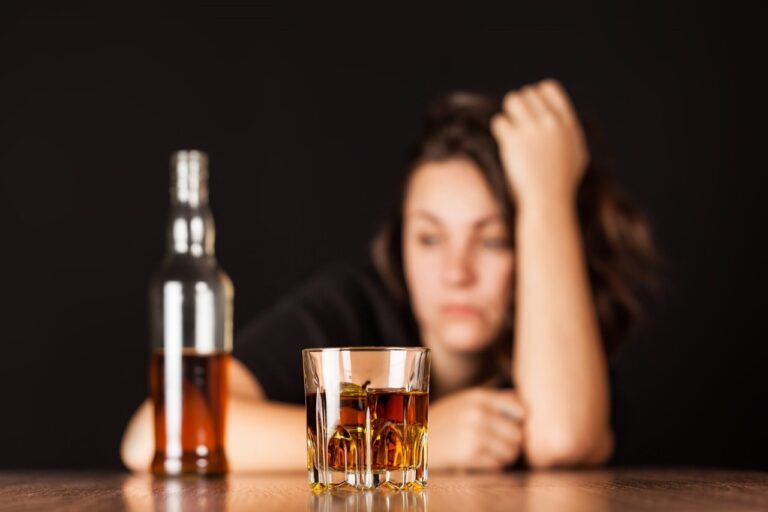 Mulher com expressão trista encarando uma garrafa de bebida alcoólica, possivelmente sofre de sintomas de dependência química