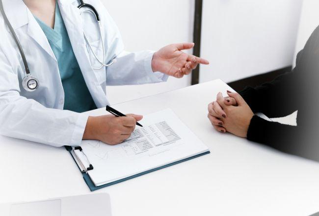 M&eacute;dica apresentando um documento a um paciente durante consulta em consult&oacute;rio