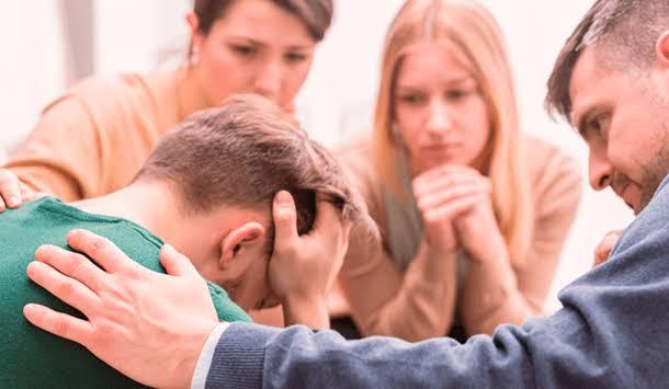 Grupo de pessoas acolhendo um homem sentado com o rosto entre as m&atilde;os durante um atendimento