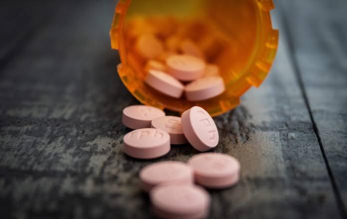 Frasco de medicamento aberto com comprimidos cor-de-rosa espalhados sobre uma superf&iacute;cie de madeira